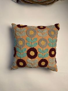 a decorative pillow is sitting on a white surface next to a basket with an orange and blue flower design