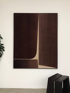 an abstract painting hangs on the wall next to a black chair and potted plant