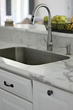 a white kitchen with marble counter tops and stainless steel sink faucet in the center