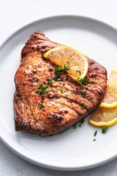 a piece of steak with lemon and parsley on a white plate, ready to be eaten