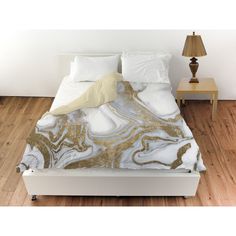 a bed with white and gold marbled sheets on it, next to a night stand