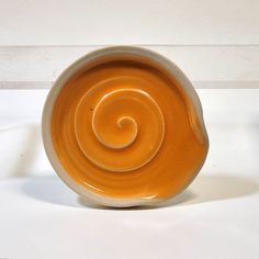 an orange and white ceramic bowl with a spiral design on the inside, sitting on a white surface