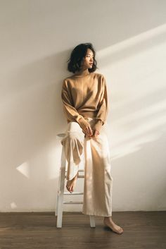 a woman sitting on a chair with her legs crossed and wearing a tan sweater over it