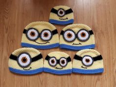 four crocheted hats with eyes on them sitting on a wooden floor next to a stuffed animal