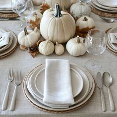 a table set with plates, silverware and white pumpkins