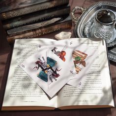 an open book sitting on top of a wooden table next to books and a tea pot