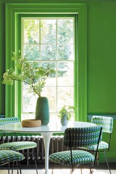 a table with four chairs and a vase on it in front of a green wall