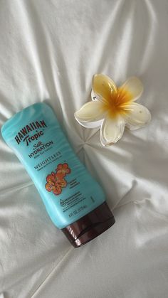 a bottle of hawaiian tanning lotion next to a flower on a white sheet