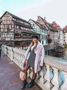 a woman is standing on a bridge in front of some buildings and holding a purse