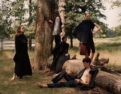 four people are sitting on logs in the grass and one person is standing up against a tree