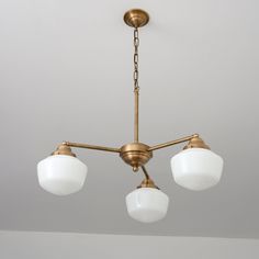 three white glass shades hang from an antique brass chandelier