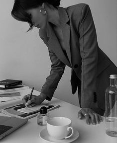 a woman writing on a piece of paper next to a laptop computer and coffee cup