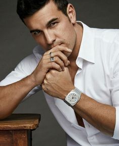 a man sitting at a table with his hand on his chin and wearing a watch