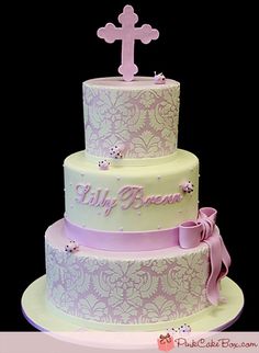 a three tiered cake with a cross on top and pink ribbon around the bottom