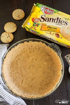 a pie with cookies next to it on top of a wooden table in front of a bag of sandies