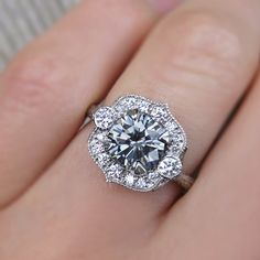 a woman's hand with a diamond ring on top of her finger and the center stone is surrounded by diamonds