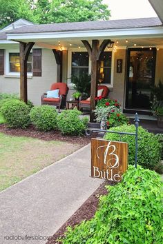 the front porch of a house with lights on and bushes growing in front of it