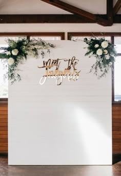 a white wall with flowers and greenery on it that says you're married