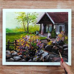 a painting of a house with flowers in the foreground and a person holding a paintbrush