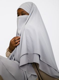 a woman in a gray hijab is holding her hands to her chest and looking off into the distance