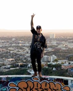 a man standing on top of a graffiti covered wall with his arms in the air