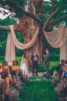 a man and woman are standing under a tree at their wedding ceremony in the park