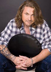 a man with long hair sitting on a toilet holding a black round object in his hands