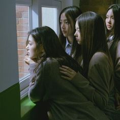 group of young women standing next to each other in front of a window