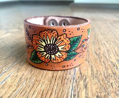 "Mod pop flowers leather bracelet. This is a cute and fun hand tooled and hand painted leather bracelet Please note each one of these is handmade so no two are exactly alike. Material Vegetable Tan leather Acrylic paint metal hardware Size 1.5\" width Please state wrist size when ordering. Please note each one of these is handmade so no two are exactly alike. Please allow 10 - 15 business days for manufacture of item, excluding shipping time. Shipping times vary and are beyond our ability to con Hand Tooled Leather Bracelet For Gift, Hand Painted Adjustable Cuff Bracelet As Gift, Adjustable Hand Painted Leather Bracelet Gift, Handmade Brown Flower Bracelets, Adjustable Hand Painted Leather Jewelry, Hand Painted Bohemian Cuff Bracelet As A Gift, Bohemian Style Hand Painted Cuff Bracelet As Gift, Bohemian Hand Painted Cuff Bracelet As Gift, Unique Hand Tooled Brown Leather Bracelet