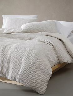 an unmade bed with white sheets and pillows on top of it, in front of a gray wall