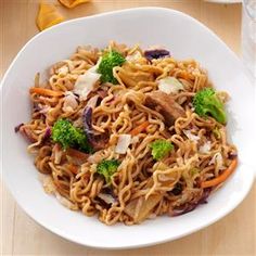 a bowl of noodles with broccoli, carrots and other vegetables on a table