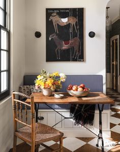 a table with fruit and flowers on it in front of a painting hanging above the couch