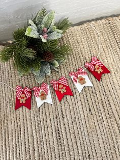 a christmas decoration with red and white ribbon, pine cone ornaments and greenery in the background