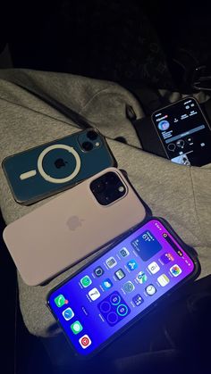 three cell phones sitting next to each other on top of a bed in the dark