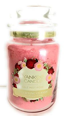 a pink candle with roses on it sitting in a glass jar next to a white wall