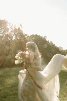 a woman in a white dress is holding flowers and walking through the grass with her horse