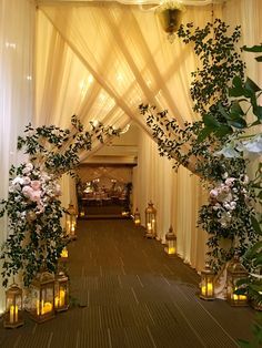 an archway decorated with candles and flowers in front of a white drapeed ceiling