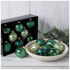 a bowl filled with green christmas ornaments next to a black box