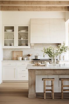 a kitchen with white cabinets and counter tops next to two stools in front of an island