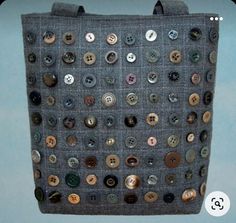 a handbag made out of buttons hanging from a hook on a blue wall in front of a light blue background