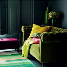 a living room with green couches and colorful rugs on the floor in front of black walls