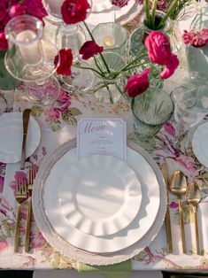 the table is set with white plates, silverware and pink flowers in vases