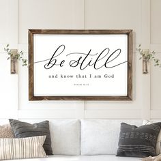 a living room with a white couch and framed poster above it that says be still and know that i am god