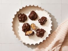 chocolate covered donuts on a white plate next to a striped towel and napkins