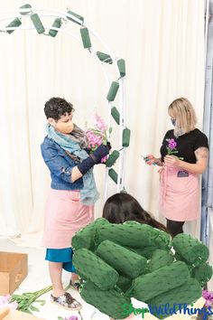 two people standing next to each other in front of a mirror with flowers on it