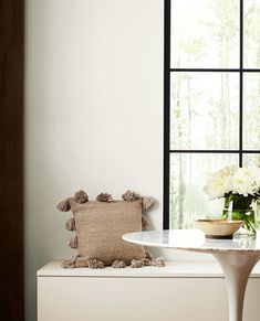 a vase with flowers sitting on top of a white table next to a large window