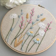 a close up of a embroidery on a piece of cloth with flowers in the background