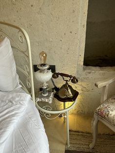 an old fashioned telephone sits on a small table next to a bed with white sheets