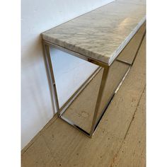 a white marble table with metal legs on a wooden floor next to a white wall