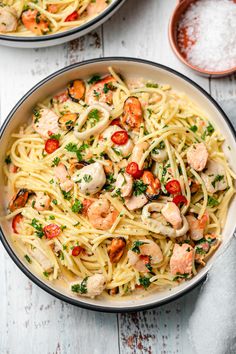 two bowls filled with pasta and shrimp on top of a white wooden table next to sauce